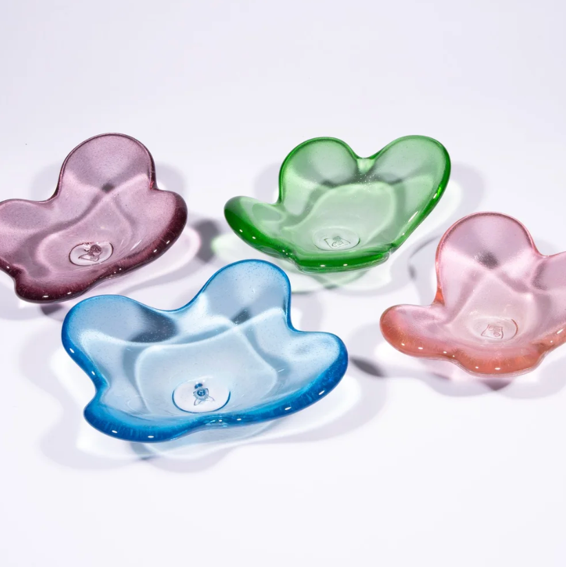 Four Cloud Dish bowls by Tyler Barry Design in purple, green, blue, and pink sit on a white surface. Each features hand-blown glass with a glossy, translucent finish and an organic, petal-like shape.