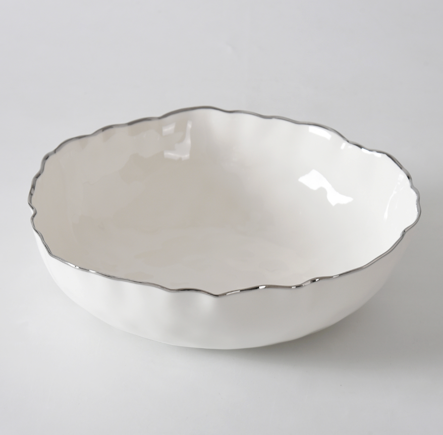 The PAMPA BAY Portofino Plata Bowl, a white porcelain medium serveware piece with a wavy silver trim, rests elegantly on a white surface.