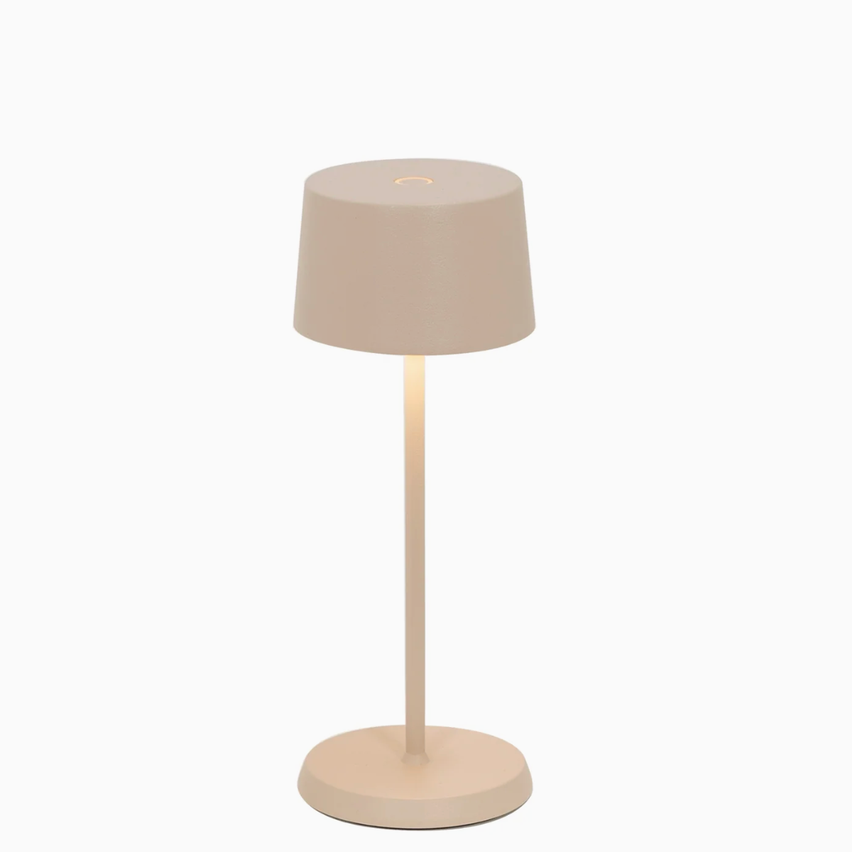 The Zafferano Olivia Pro Micro Table Lamp in Sand has a minimalist design with a beige cylindrical shade, slim straight stand, and round base, all matching. Shown switched on against a white background, it emits warm downward light.