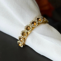 A Golden Bar Napkin Ring set of 4 featuring a gold-toned band with a row of amber crystals surrounded by clear stones, encircling a white cloth napkin.