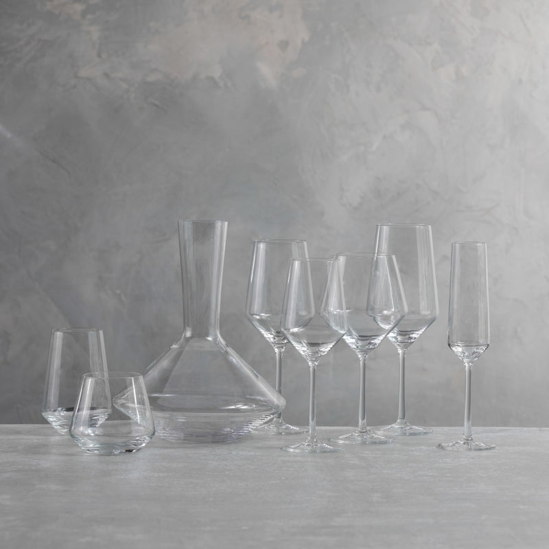 The Zwiesel Fortessa Zweisel Pure Barware set, made of durable Tritan, features a decanter, two stemless wine glasses, three wine glasses, and two champagne flutes arranged on a light surface against a textured gray background.