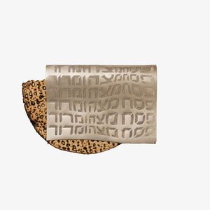 A piece of matzah is partially covered by the Apeloig Type Afikoman Bag, which features a laser-cut Hebrew design, set against a plain white background.