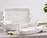 The Ivy Melamine Chip & Dip by PAMPA BAY features white shatterproof dishes with wavy edges and handles, shown on a light wood surface with linen, greenery, and lime wedges. Ideal for outdoor serving at any occasion.