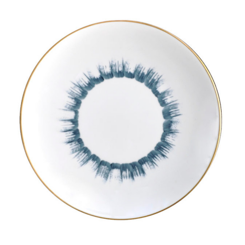 The Marie Daâge Iris 1 Dinnerware by Marie Daâge features a round white Limoges porcelain plate with a thin gold rim and a blue brushstroke-style circular pattern at the center, evoking a ring or sunburst.