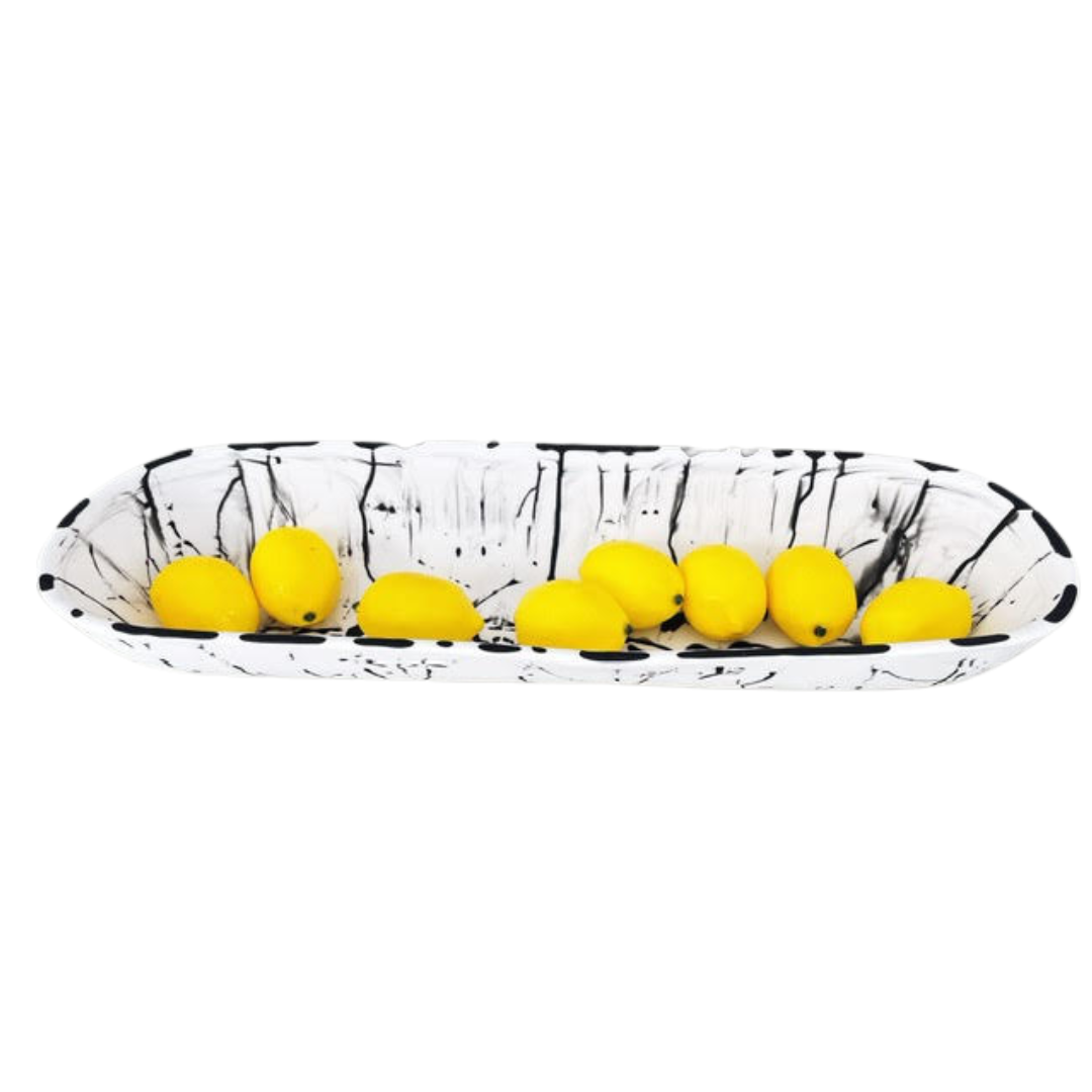 White solid and black splatter boat bowl with lemons on top.